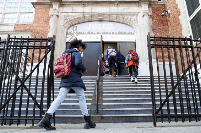 Students enter through the gates and up the steps of a high school
